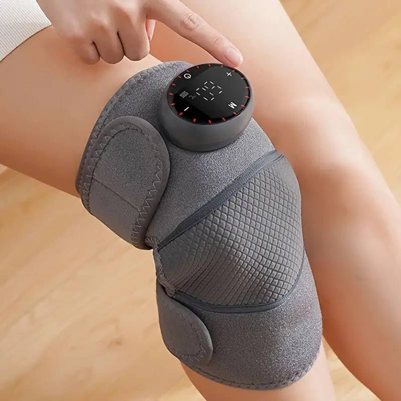 Masseur chauffant pour genou gris porté sur un genou nu, doigt touchant le panneau de commande, parquet en arrière-plan