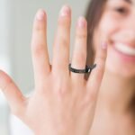 Baguier noir porté au doigt d’une femme souriante en arrière-plan