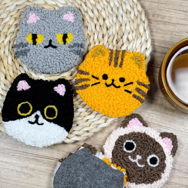 Sous-verres chats en punch needle terminés sur un set tressé à côté d’une tasse de thé