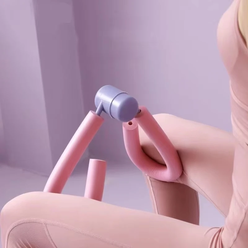 Appareil d’entraînement des cuisses rose à moyeu lilas tenu entre les jambes d’une femme pendant un entraînement à domicile