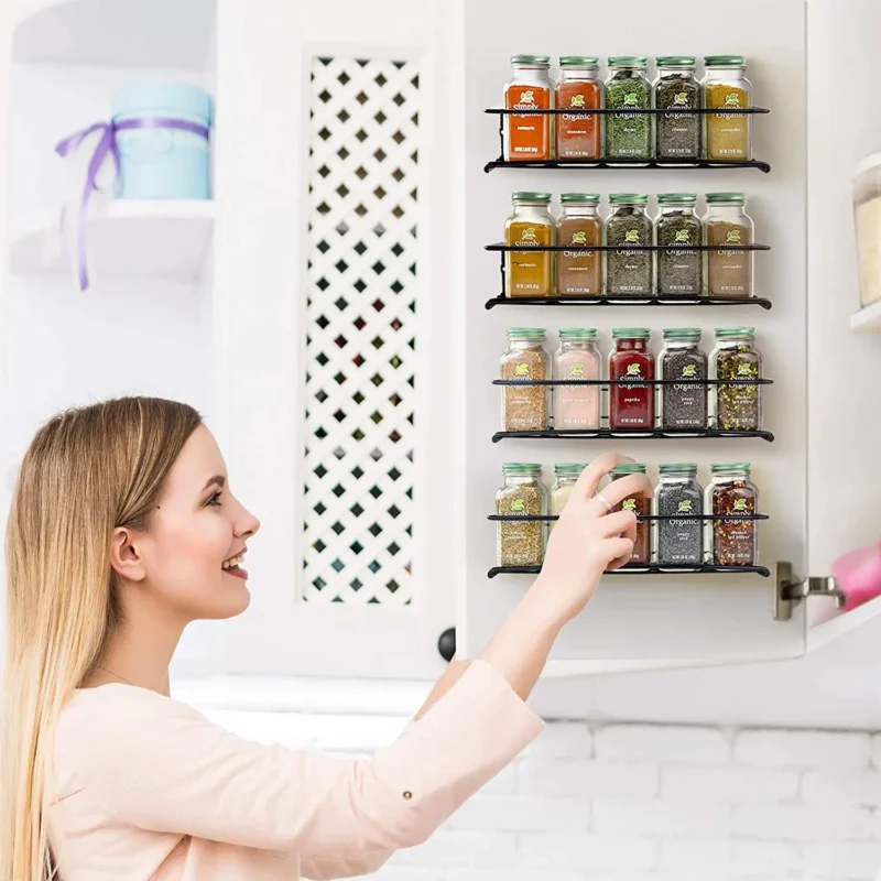 Étagères à épices murales noires fixées sur une porte de placard de cuisine, remplies de pots