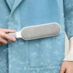 Main utilisant la brosse anti-poils sur un manteau en laine bleu couvert de poils