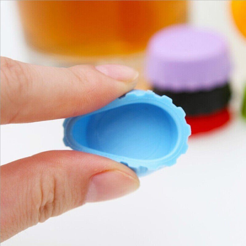 Capsule de bouteille en silicone bleue tenue entre les doigts à côté d’un verre de bière et d’autres capsules